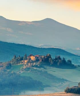 A scenic view of a Tuscan landscape featuring rolling hills and a farmhouse on a hilltop. - Olive Oil Times