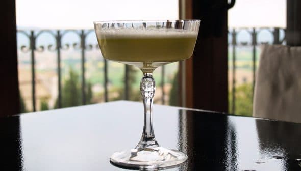 A crystal glass filled with a light green cocktail placed on a reflective surface. - Olive Oil Times