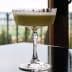 A crystal glass filled with a light green cocktail placed on a reflective surface. - Olive Oil Times