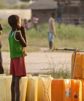 Two children standing beside yellow water containers in an outdoor setting during daylight. - Olive Oil Times