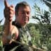 Man gesturing while standing among olive trees in an olive grove. - Olive Oil Times