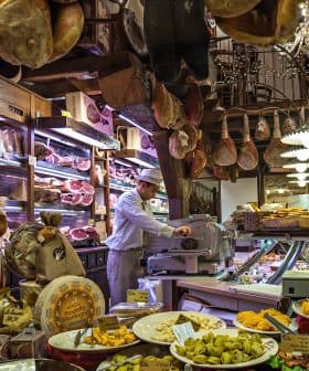 Interior of an Italian deli featuring various meats, cheeses, and a staff member slicing meat. - Olive Oil Times