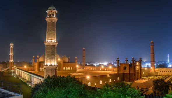 Badshahi Mosque illuminated at night with minarets and domes visible. - Olive Oil Times