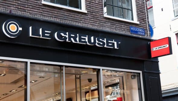 Storefront signage of Le Creuset with a black background and illuminated logo. - Olive Oil Times
