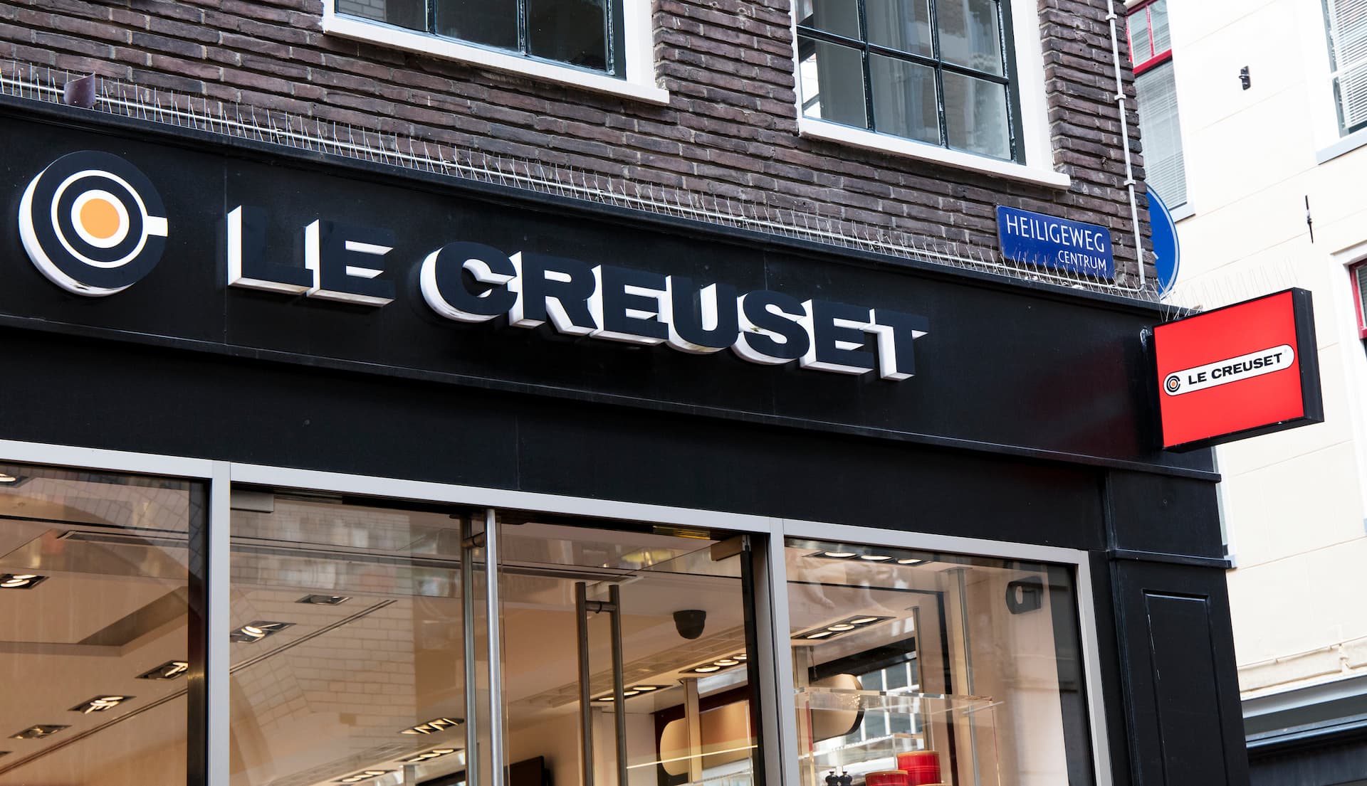 Storefront signage of Le Creuset with a black background and illuminated logo. - Olive Oil Times