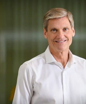 A man smiling while wearing a white shirt, standing in front of a blurred background. - Olive Oil Times
