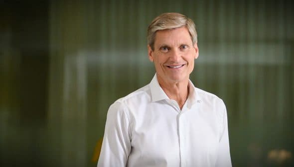 A man smiling while wearing a white shirt, standing in front of a blurred background. - Olive Oil Times