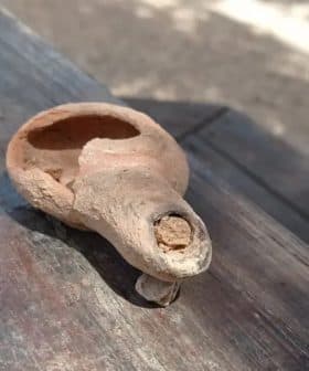 An ancient clay olive oil lamp with a spout and a round body resting on a wooden surface. - Olive Oil Times