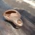 An ancient clay olive oil lamp with a spout and a round body resting on a wooden surface. - Olive Oil Times