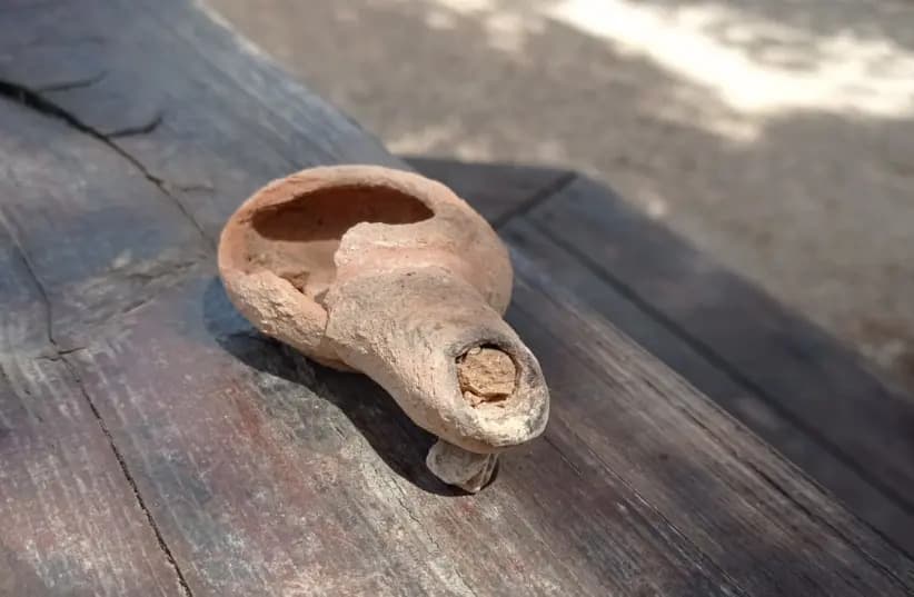 An ancient clay olive oil lamp with a spout and a round body resting on a wooden surface. - Olive Oil Times
