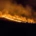 A hillside engulfed in flames during a wildfire, with smoke billowing into the night sky. - Olive Oil Times