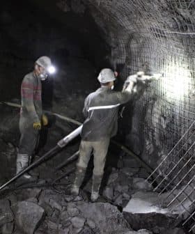 Two miners working in a dark underground mine with safety gear and tools. - Olive Oil Times