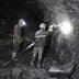 Two miners working in a dark underground mine with safety gear and tools. - Olive Oil Times