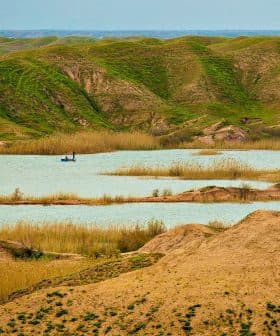 A serene landscape featuring green hills, a water body, and a small boat in the distance. - Olive Oil Times