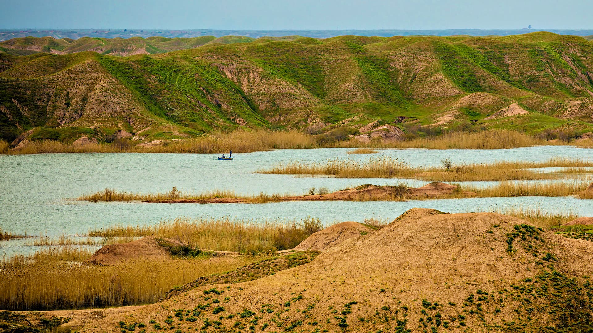 A serene landscape featuring green hills, a water body, and a small boat in the distance. - Olive Oil Times