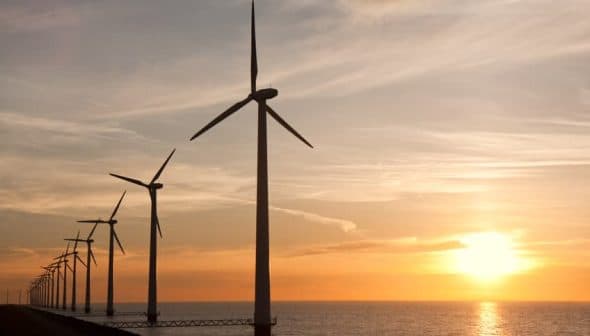 Row of wind turbines along the coastline during sunset with a colorful sky. - Olive Oil Times
