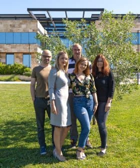 Five individuals standing together outdoors in front of a modern building with greenery. - Olive Oil Times