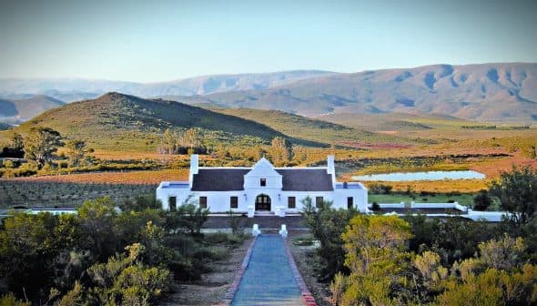 White building of Galenia Estate with mountains and greenery in the background. - Olive Oil Times
