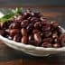 A white bowl filled with a variety of dark olives, garnished with a sprig of olive leaves. - Olive Oil Times