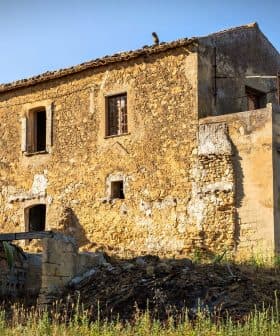 Abandoned stone house with a rustic exterior and overgrown vegetation in a rural area. - Olive Oil Times