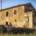 Abandoned stone house with a rustic exterior and overgrown vegetation in a rural area. - Olive Oil Times