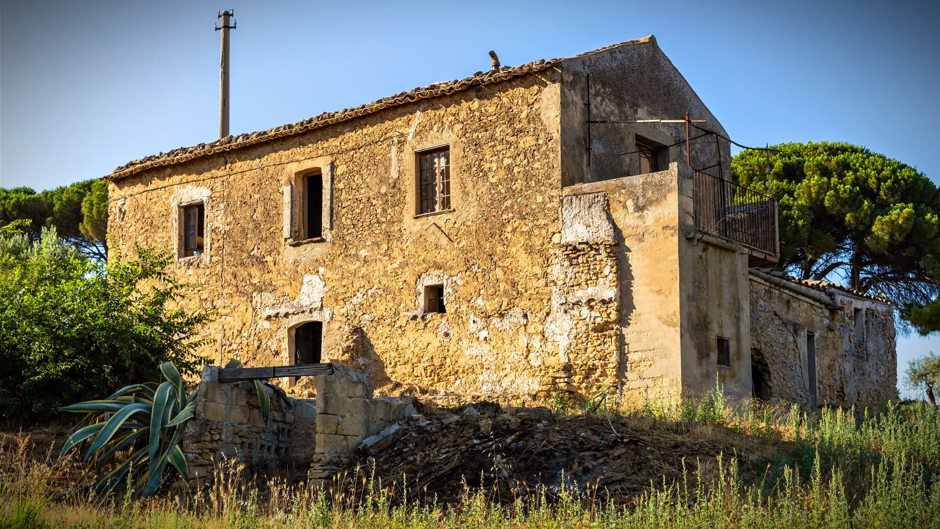 Abandoned stone house with a rustic exterior and overgrown vegetation in a rural area. - Olive Oil Times