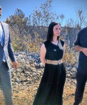 Three individuals standing outdoors, two in formal attire and one in work uniform, engaged in conversation. - Olive Oil Times