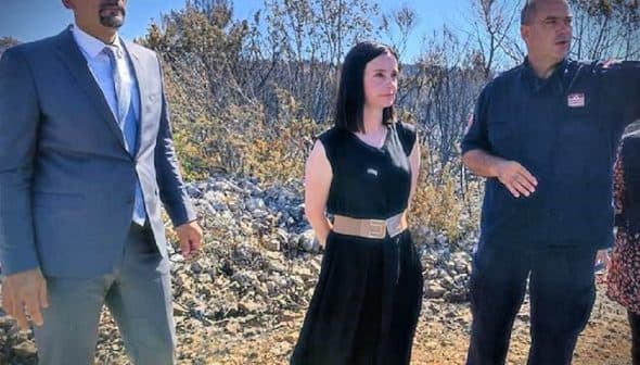 Three individuals standing outdoors, two in formal attire and one in work uniform, engaged in conversation. - Olive Oil Times