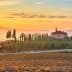 A scenic view of a house surrounded by cypress trees in a Tuscan landscape at sunrise. - Olive Oil Times