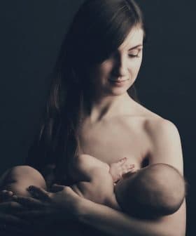 A mother gently cradling her baby in a dark background, both appearing calm and serene. - Olive Oil Times