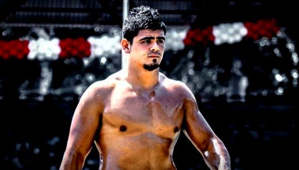 Shirtless male athlete with short dark hair standing outdoors, looking to the side. - Olive Oil Times