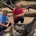 Two men kneeling beside a tree stump in a dry outdoor setting with fallen branches. - Olive Oil Times