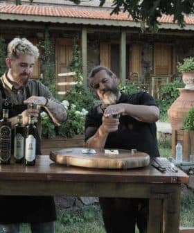 Two men participating in an olive oil tasting session at a wooden table outdoors. - Olive Oil Times
