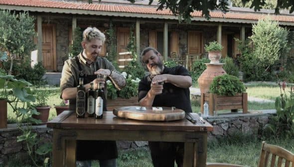Two men participating in an olive oil tasting session at a wooden table outdoors. - Olive Oil Times