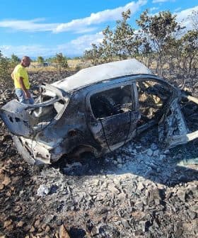 A burnt car surrounded by charred ground and sparse vegetation after a fire incident. - Olive Oil Times