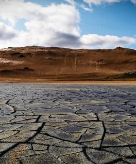 Dry, cracked earth surface with a mountainous background under a cloudy sky. - Olive Oil Times