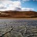 Dry, cracked earth surface with a mountainous background under a cloudy sky. - Olive Oil Times