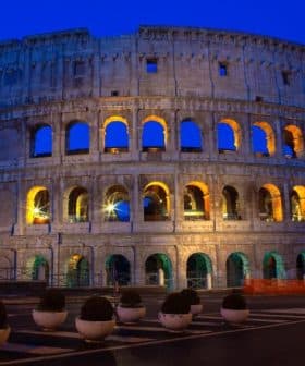 The Colosseum in Rome illuminated at dusk with a blue sky backdrop and lit arches. - Olive Oil Times