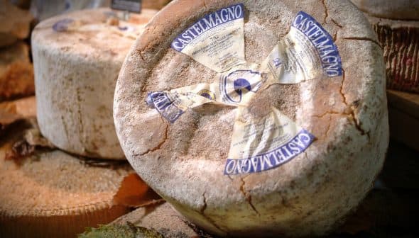 Round wheel of Castelmagno cheese with a blue and white label on a wooden surface. - Olive Oil Times
