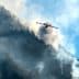 An aircraft releasing water to combat a wildfire in a mountainous region with smoke rising from the ground. - Olive Oil Times