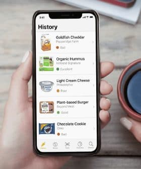 Person holding a smartphone displaying a food review app with various food items and ratings. - Olive Oil Times