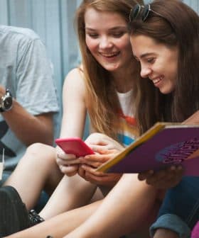 Four young individuals sitting together, sharing a moment while looking at a smartphone. - Olive Oil Times