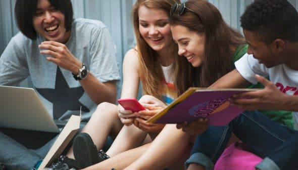 Four young individuals sitting together, sharing a moment while looking at a smartphone. - Olive Oil Times