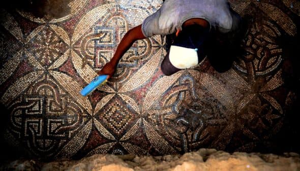An archaeologist using a tool to clean an intricate ancient mosaic floor. - Olive Oil Times
