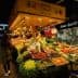 A vibrant market stall displaying a variety of fruits and vegetables, including greens, tomatoes, and grapes. - Olive Oil Times