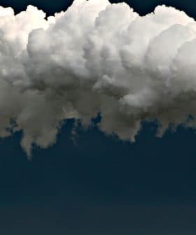 Tall industrial smokestack emitting large clouds of white smoke against a dark sky. - Olive Oil Times