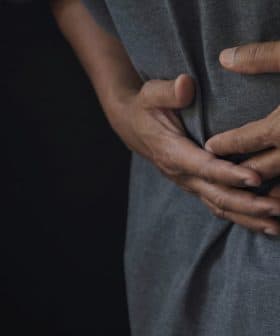 Individual wearing a gray shirt, holding their stomach with both hands, indicating discomfort. - Olive Oil Times