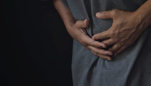 Individual wearing a gray shirt, holding their stomach with both hands, indicating discomfort. - Olive Oil Times