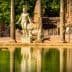 Statue of a Roman warrior holding a shield near ancient columns and water reflection. - Olive Oil Times
