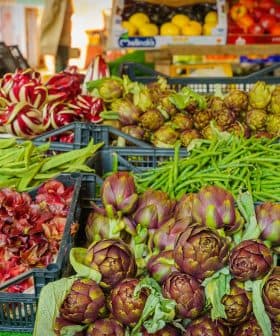 Display of assorted fresh vegetables and fruits including artichokes, green beans, and oranges at a market. - Olive Oil Times